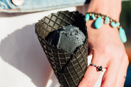 young woman holds in hand dark black cone ice-cream. Close-up portrait female with red lips.の写真素材