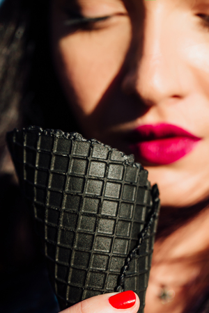 young woman eating dark black cone ice-cream. Close-up portrait female with red lips.の写真素材