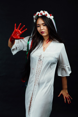 Portrait of a bloody beautiful Asian girl on Halloween. White dress-robe, ethnic wreath of flowers.の写真素材