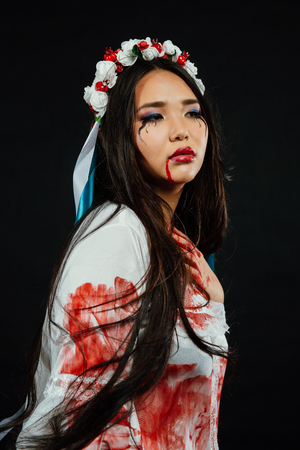 Portrait of a bloody beautiful Asian girl on Halloween. White dress-robe, ethnic wreath of flowersの写真素材