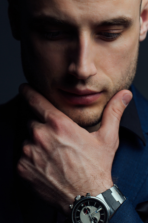 Studio portrait of young sexy man in black shirt, holding hands in chin, looking down with humility.の写真素材