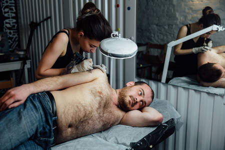 young brunette girl Professional tattoo artist . master draws on mans shoulder arm.の写真素材