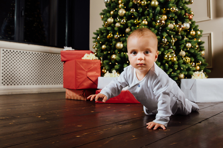 small baby is sitting on the couch, against the background of a Christmas tree.の写真素材