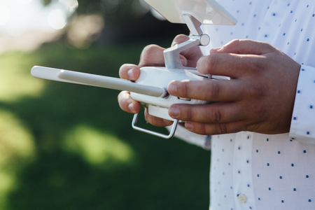 Man holds a drone remote controller in his hands. Close-up of quad copter RC with antennas during flight. Pilot takes aerial photos and videos with quad. No faceの写真素材