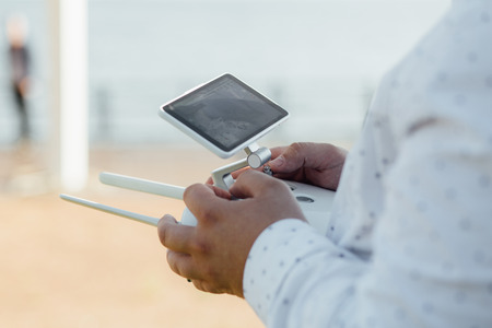 Man holds a drone remote controller in his hands. Close-up of quad copter RC with antennas during flight. Pilot takes aerial photos and videos with quad. No faceの写真素材