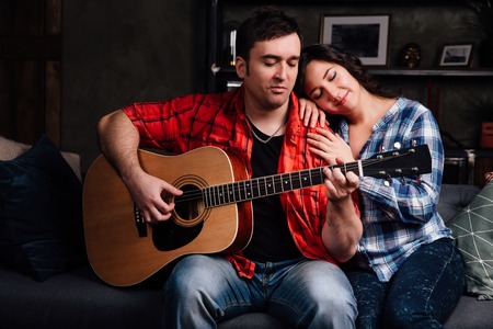 couple is sitting on the couch with a guitar. Long hair of a brunette with an acoustic guitar.の写真素材