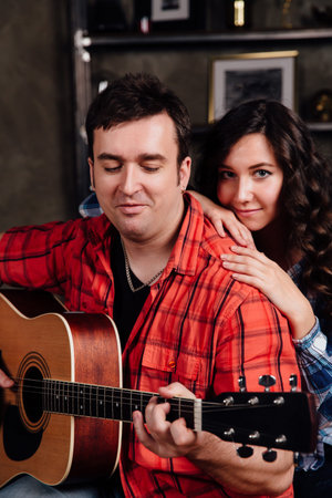 couple is sitting on the couch with a guitar. Long hair of a brunette with an acoustic guitar.