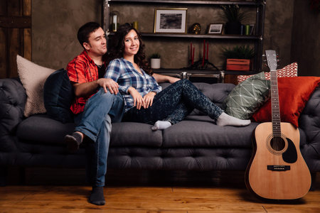 couple is sitting on the couch with a guitar. Long hair of a brunette with an acoustic guitar.