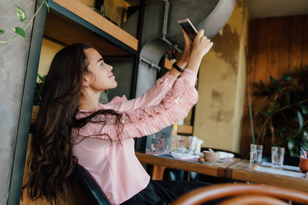 Beautiful long-haired brunette girl doing selfie at a cafe. Photographed, fooled and fun.の写真素材