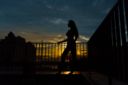 Silhouette of sexy girl in mini dress on heels, on city background. Sunset, railing, fence, perfect figure female.の写真素材