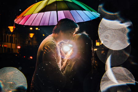 young couple under an umbrella kisses at night on a city street.の写真素材