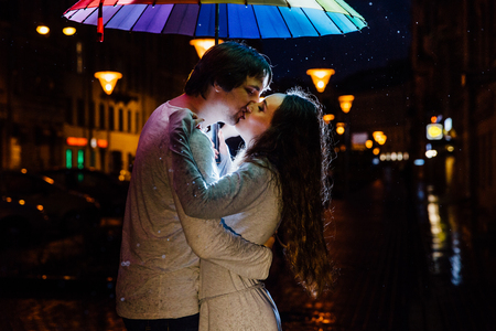 young couple under an umbrella kisses at night on a city street.の写真素材