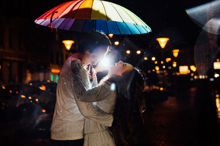 young couple under an umbrella kisses at night on a city street.の写真素材