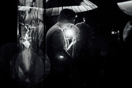 young couple under an umbrella kisses at night on a city street.の写真素材