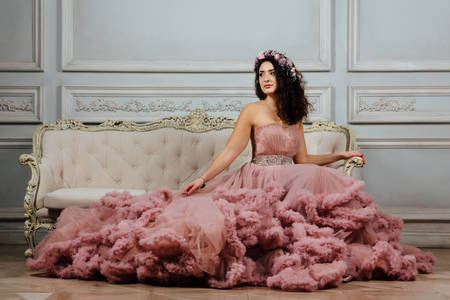 Luxurious sexy girl in an evening cloudy dress sitting on a sofa in the studio interior.の写真素材