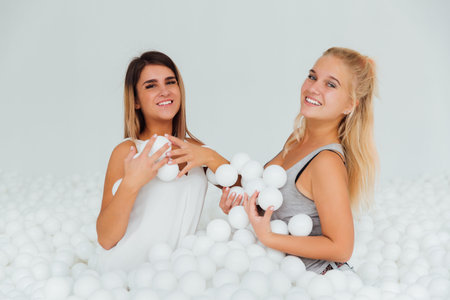 Portrait Happy Girlfriends stand surrounded by white plastic balls in the dry pool.の写真素材