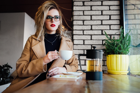 Beautiful fashionable stylish girl sits in a cafe with a cup of coffee.の写真素材