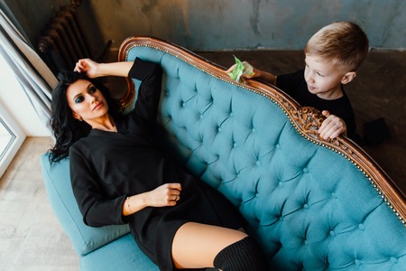 Beautiful brunette mom hugging her son lying on the sofa. Family. mother and her cute boy. black clothes.の写真素材