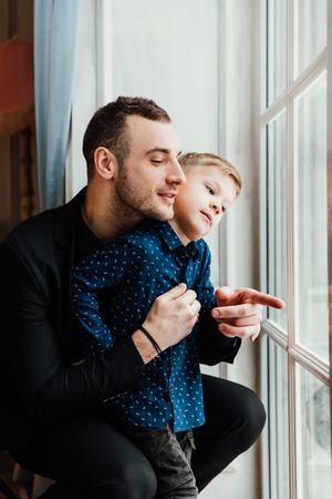 Photo of happy man and his son sitting by the windowの写真素材