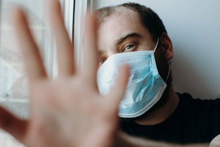 Coronavirus. Sick man of corona virus looking through the window and wearing mask protection.の写真素材
