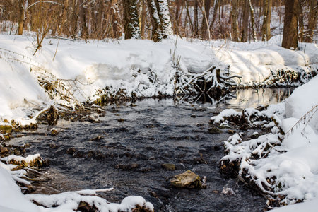 View of a small river in the forest running in the winter among white snow