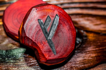Rune Fehu red color carved from wood on a wooden background - Elder Futhark