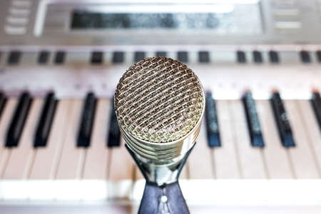 Silver microphone on rack close-up. Keyboard synthesizer in the backgroundの写真素材