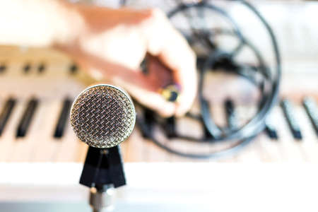 Silver microphone on rack closeup. Keyboard synthesizer and audio wires in the background. Connector for the microphoneの写真素材