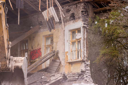 Demolition of an old brick building with an excavator bucketの写真素材
