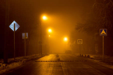 The road at night illuminated by dim lanterns during a thick fog, foggy eveningの写真素材