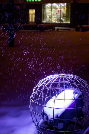 Falling snow over the blue spotlight on the street at night
