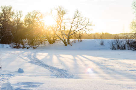 Sunny winter landscape on a sunny day. Trail on the frozen river. Snowy nature at sunset
