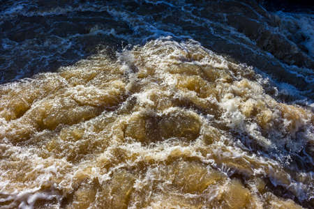 A stormy stream of water on a river dam, water with splashes and foam on the rift