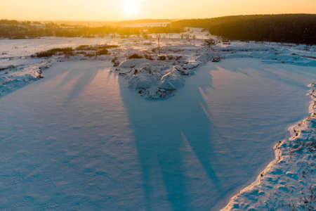 Frozen and snow-covered pond in winter against the backdrop of a bright sunset