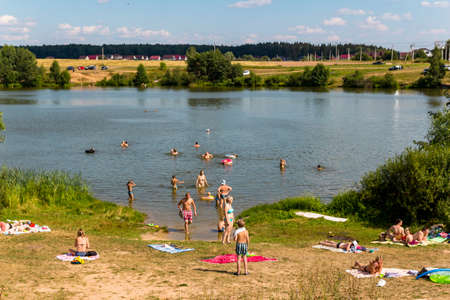 A simple wild beach on a small rural lake, people swim in a pond on a hot summer day: Mashkovo village, Zhukovsky district, Kaluga region, Russia - July 2021のeditorial素材