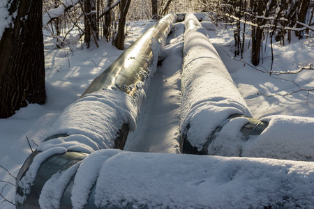 Large pipes with hot water laid outdoors above the ground, pipes covered with snow in winterの写真素材