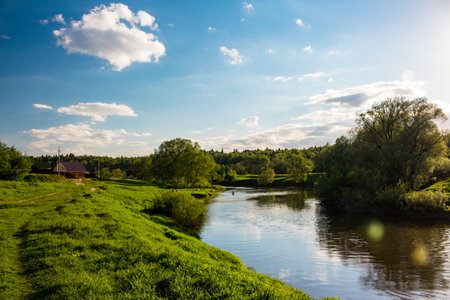 Picturesque pastoral landscape with a view of a river in the countryside, houses and bathers in the backgroundの写真素材