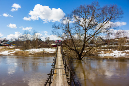 Village footbridge across the river flooded in the spring flood, rural landscape at the end of...