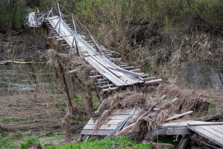 Broken and skewed footbridge after a heavy flood on a river in the countrysideの写真素材