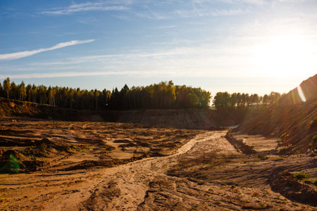 Expansive sandy quarry landscape under a bright sky with distant trees. Warm sunlight illuminates...
