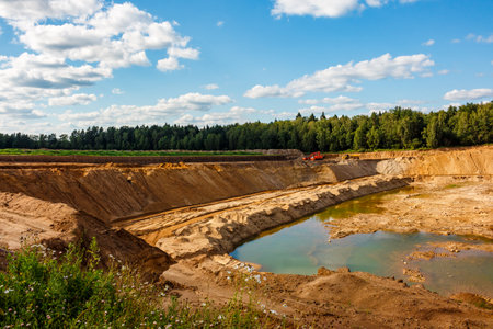 Expansive sand quarry, a huge open-pit, with heavy machinery and a water-filled basin. Earthworks in...