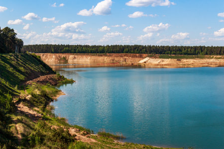 Azure waters of a large lake shimmer under a sunny sky. Lush green hills and distant pine forest...