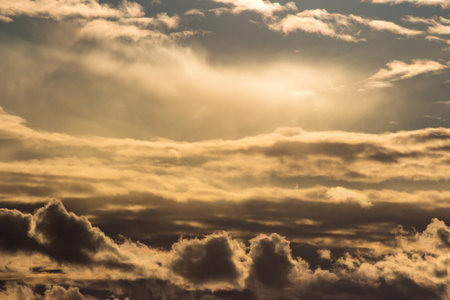 Dramatic golden clouds fill the sky, illuminated by soft sun rays breaking through. An atmospheric weather scene creates a stunning natural backgroundの写真素材