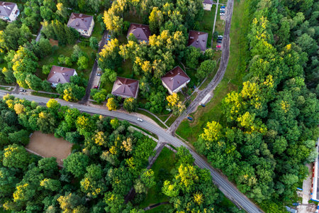 Aerial view of lush green suburban area featuring residential houses with brown roofs, nestled among abundant trees and winding roads. A peaceful, eco-friendly living spaceの写真素材