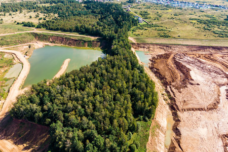 Aerial view of an active sand quarry with light green water and surrounding dense forest....