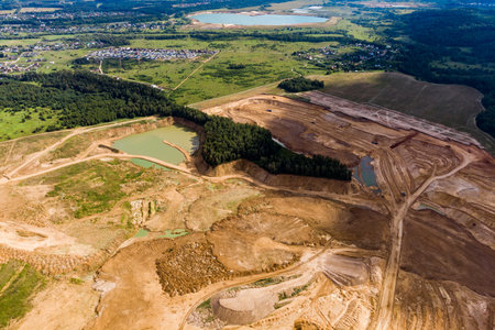 Aerial view of a vast open-pit sand quarry with active excavation, brown earth, industrial machinery, and water pools, contrasting with green fieldsの写真素材