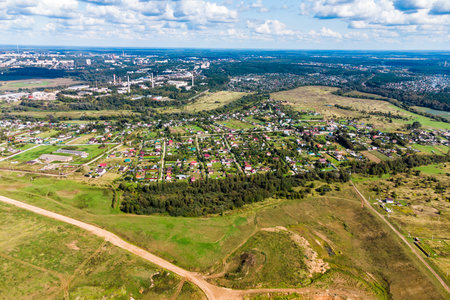 Aerial view of a suburban village with many small houses and green areas. A city skyline is visible...