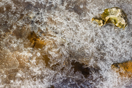 Gorgeous frost patterns on a partially frozen stream, revealing amber water and stones below....