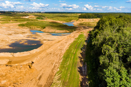 Expansive open-pit sand quarry, showing extraction activity with sandy terrain and pools of water....