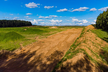 Vast sand quarry expansion with fresh overburden removal, showing new earthy tracts, green fields,...